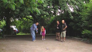 Un grupo de personas jugando a un juego al aire libre, sobre suelo de tierra, con árboles de fondo.