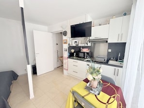A compact kitchen with white cabinets, a microwave, and a flat-screen TV. - Pleasant studio facing sea with beach access and parking (Le Barcarès)
