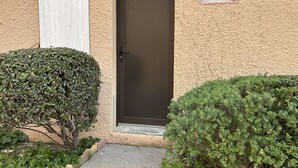 A building with a textured beige exterior, a dark brown door, and a small window above it. - Seaside house 3 rooms, terrace, pets allowed (Fleury-Saint-Pierre-la-Mer)
