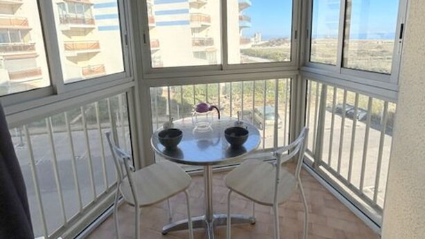 Ein kleiner Balkon mit Tisch und zwei Stühlen, Blick auf eine Wohngegend mit mehreren Gebäuden.