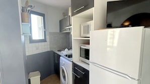 Een kleine keuken met een wasmachine, een magnetron en een koelkast.