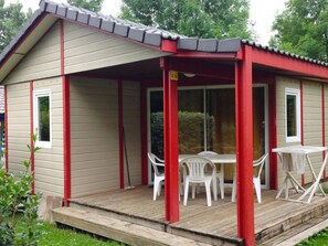 A small, single-story building with a covered porch, a table and chairs, and a window.