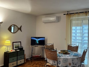 Ein Wohnzimmer mit Fernseher, einem spiegelartigen Fisch, einem Esstisch mit Stühlen und einer Klimaanlage.