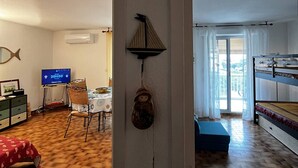 Et værelse med fjernsyn, spisebord, stole, sofa, køjeseng og vægmonteret hylde.
