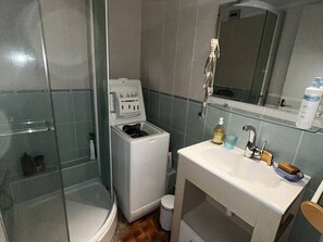 Ett badrum med en duschkabin i glas, en vit toalett, ett handfat med spegel och en tvåldispenser.