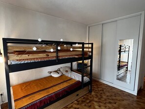 En våningssäng med en träram, en hylla längst ner med en kudde och en spegel på höger sida.