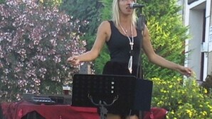 A person standing on a stage with a microphone, surrounded by greenery and a building in the background. - 30m² Chalet with Terrace for 6 People (Capvern)