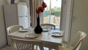Comedor con una mesa preparada para dos personas, sillas blancas, un jarrón con flores y vistas al exterior.