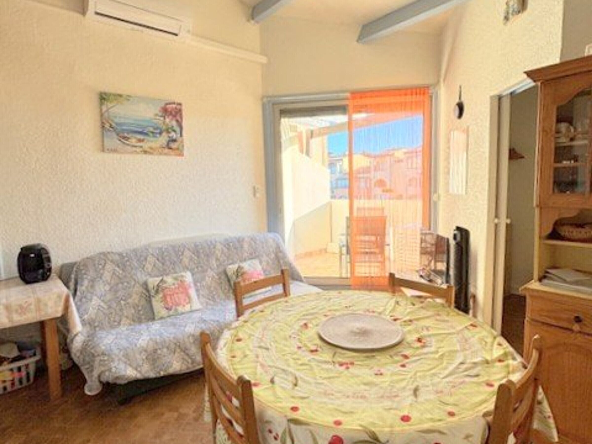 A cozy room with a sofa, a dining table with chairs, a cabinet, and a painting on the wall.