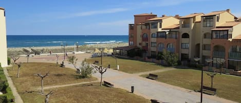 Ein Hotel direkt am Strand mit einem gepflasterten Weg, Bänken und Blick auf das Meer.