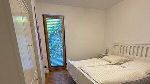 Un dormitorio con piso de madera, una cama con ropa de cama blanca, una mesita de noche y un armario.