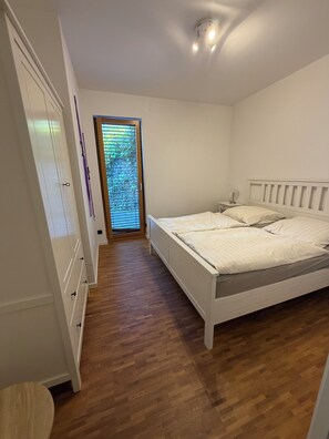 Ein Schlafzimmer mit Holzboden, einem Bett mit weißer Bettwäsche, einem Nachttisch und einem Kleiderschrank.