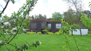 Una casa moderna de dos pisos con techo rojo, rodeada de césped cuidado y árboles.