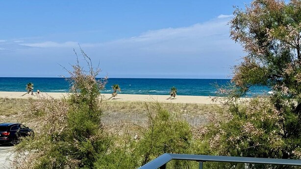 Una playa con cielos despejados y aguas tranquilas, rodeada de vegetación y un coche estacionado.