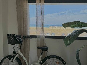 Una bicicleta apoyada en una ventana con vistas a la playa y un estacionamiento.