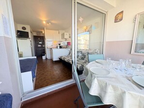 Ein kompakter Raum mit Esstisch für zwei Personen, einer Küchenzeile, einer Couch und einer Glastür zum Balkon.