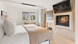 Quarto com cama, lareira, televisão e janela com vista.