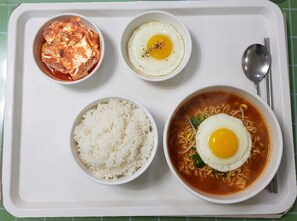 A tray with four food items: kimchi, a fried egg, rice, and ramen with a fried egg.