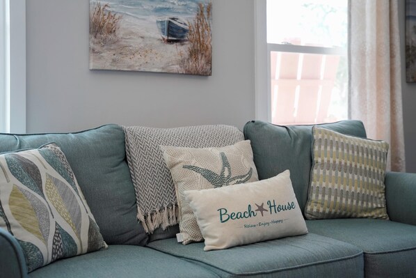 A teal sofa with patterned cushions and a beach-themed pillow. - Mexico Beach w/Low Speed Vehicle (Mexico Beach)