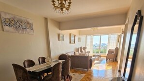 Un amplio salón con una mesa de comedor, sillas, una araña y un ventanal que ofrece vistas de la ciudad.