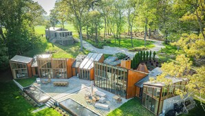 Una casa moderna con varias habitaciones con paredes de vidrio, una terraza amplia y un jardín circundante.