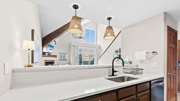 A modern kitchen with a white countertop, dark wooden cabinets, a stainless steel sink, and two wicker pendant lights. - Spacious Family-Friendly Condo With Updated Finishes (Frisco)