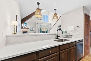 Una cucina moderna con un piano di lavoro bianco, mobili in legno scuro, un lavandino in acciaio inossidabile e due lampade a sospensione in vimini.