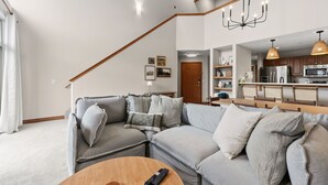 A modern living room with a grey sectional sofa, a wooden coffee table, and a chandelier. - Spacious Family-Friendly Condo With Updated Finishes (Frisco)