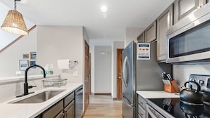 A modern kitchen with stainless steel appliances, a white countertop, and a wooden floor. - Spacious Family-Friendly Condo With Updated Finishes (Frisco)