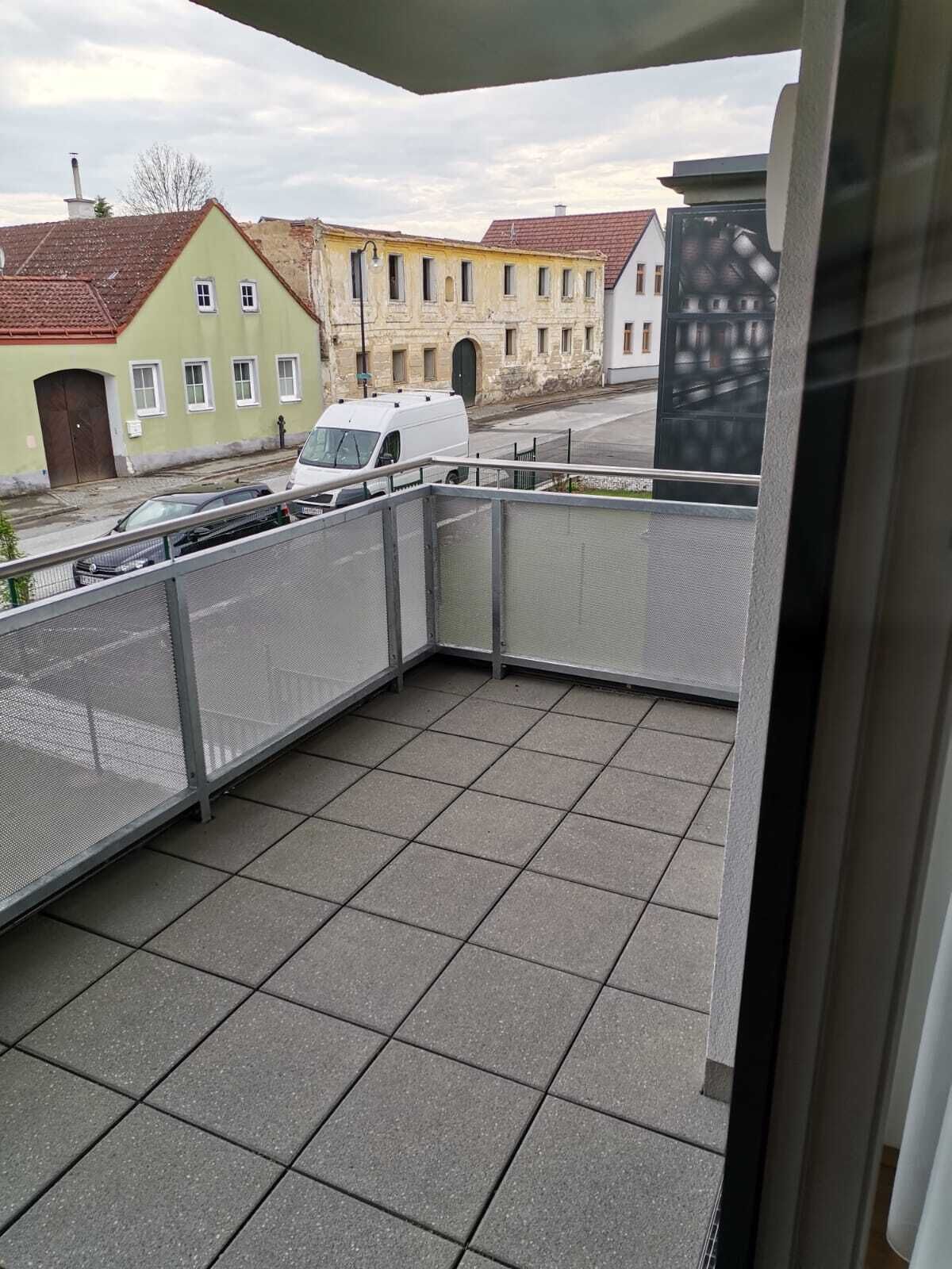 Een balkon met uitzicht op een straat, een geparkeerde witte bus en gebouwen op de achtergrond.