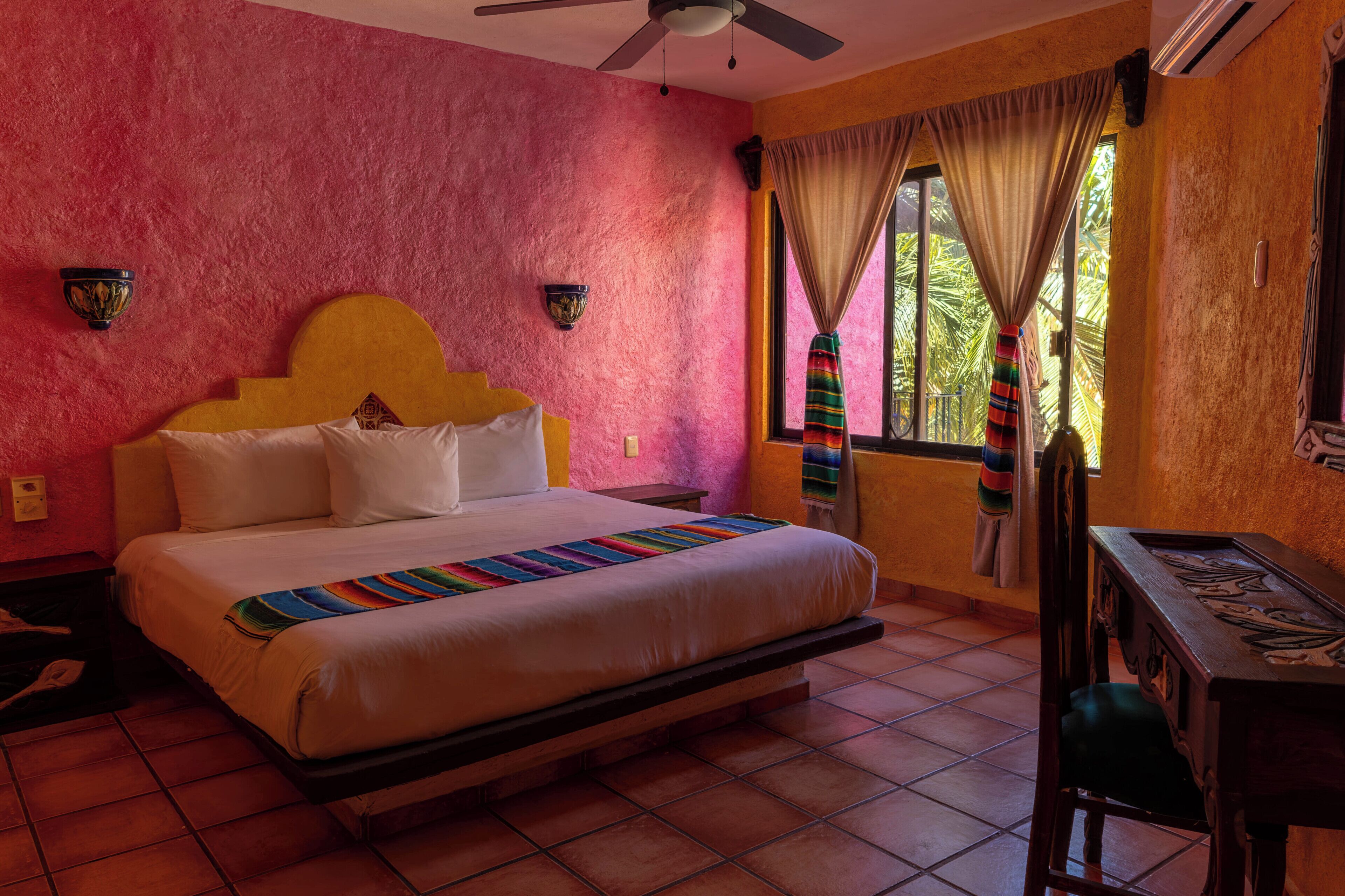 A room with a bed, a desk, a chair, a ceiling fan, and a window with curtains.