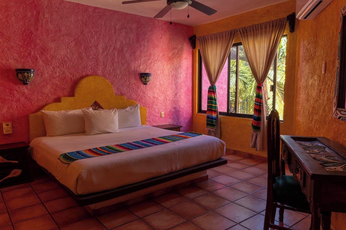 A room with a bed, a desk, a chair, a ceiling fan, and a window with curtains.