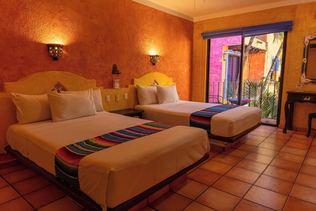 A hotel room with two beds, a balcony with a view, and a small table with a chair.