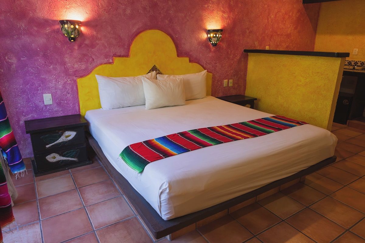 A bed with a colorful blanket, a headboard, and two wall-mounted lights.
