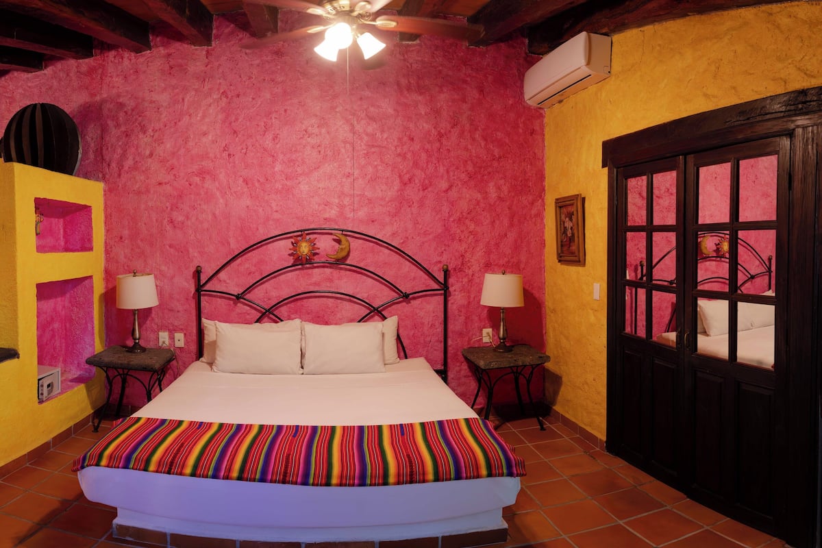 A bedroom with a bed, two bedside tables, a ceiling fan, and a window with a view.