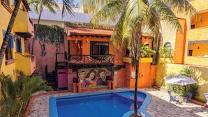 A courtyard with a swimming pool, palm trees, and colorful buildings. - Hotel Hacienda Maria Bonita (Playa del Carmen)