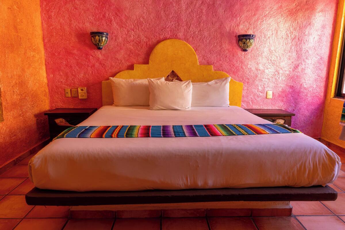 A bed with a headboard, pillows, and a colorful blanket.