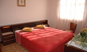 A bedroom with a bed, two pillows, a nightstand, a chair, a window with curtains, and a small table with a plant. - Cozy Villa With a Fenced Garden (Lignano Sabbiadoro)