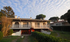 A two-story house with a balcony, a garden, and a staircase leading to the upper floor. - Cozy Villa With a Fenced Garden (Lignano Sabbiadoro)