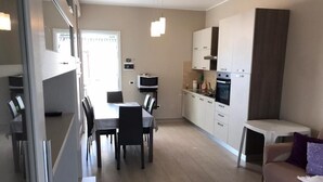 A modern kitchen with white cabinets, a dining area with a table and chairs, and a sofa in a living area. - Sicily house 100 mt from the sea, garden, climate, terrace, laundry room (Cervia)