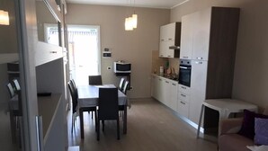 A modern kitchen with white cabinets, a dining area with a table and chairs, and a small seating area with a sofa. - Sicily house 100 mt from the sea, garden, climate, terrace, laundry room (Cervia)
