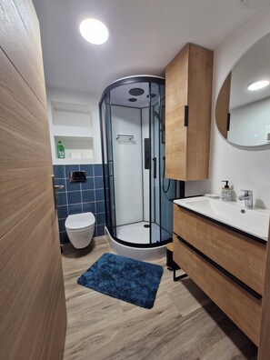 Ein modernes Badezimmer mit einer Duschkabine, einer weißen Toilette, einem hölzernen Waschtisch und einem blauen Teppich.
