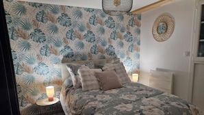 Ein Schlafzimmer mit floralem Bettbezug, einem Kopfteil und einem Nachttisch mit Lampe.