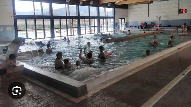 Ein Hallenbad mit mehreren Bahnen, großen Fenstern und einer Holzbalkendecke.