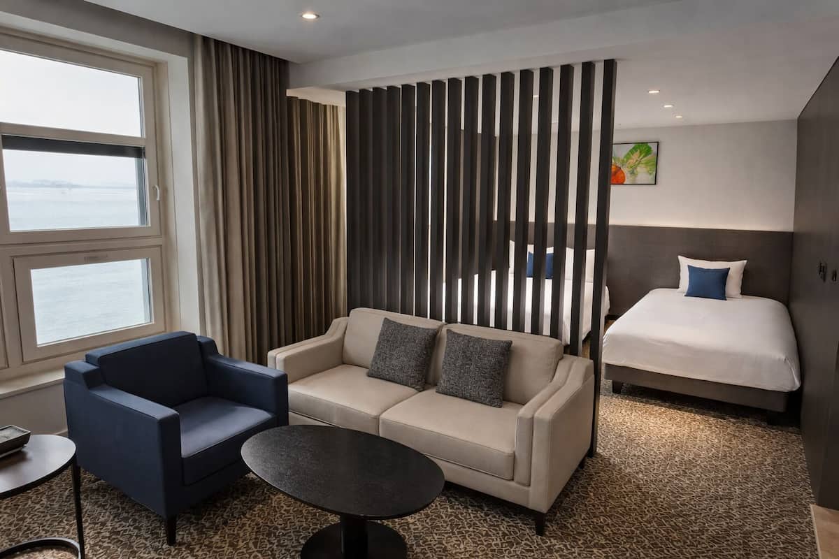 A hotel room with a sofa, a chair, a small table, a bed, and a view of the water.