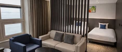 A hotel room with a sofa, a chair, a small table, a bed, and a view of the water.