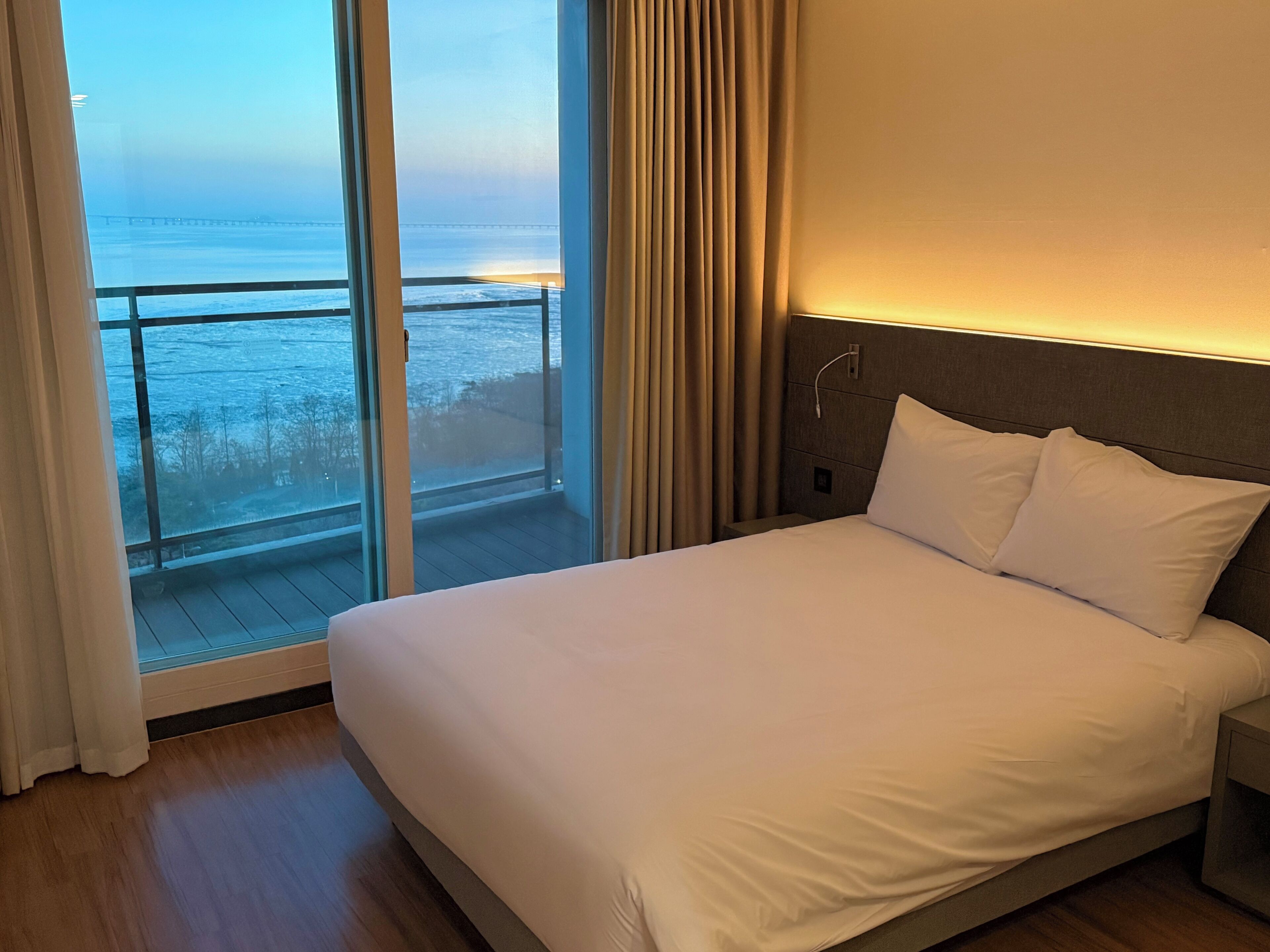 Une chambre d’hôtel avec un grand lit, une table de chevet et une vue sur l’océan par une porte-fenêtre coulissante.