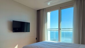Een hotelkamer met een bed, een aan de muur bevestigde televisie en een groot raam met gordijnen.