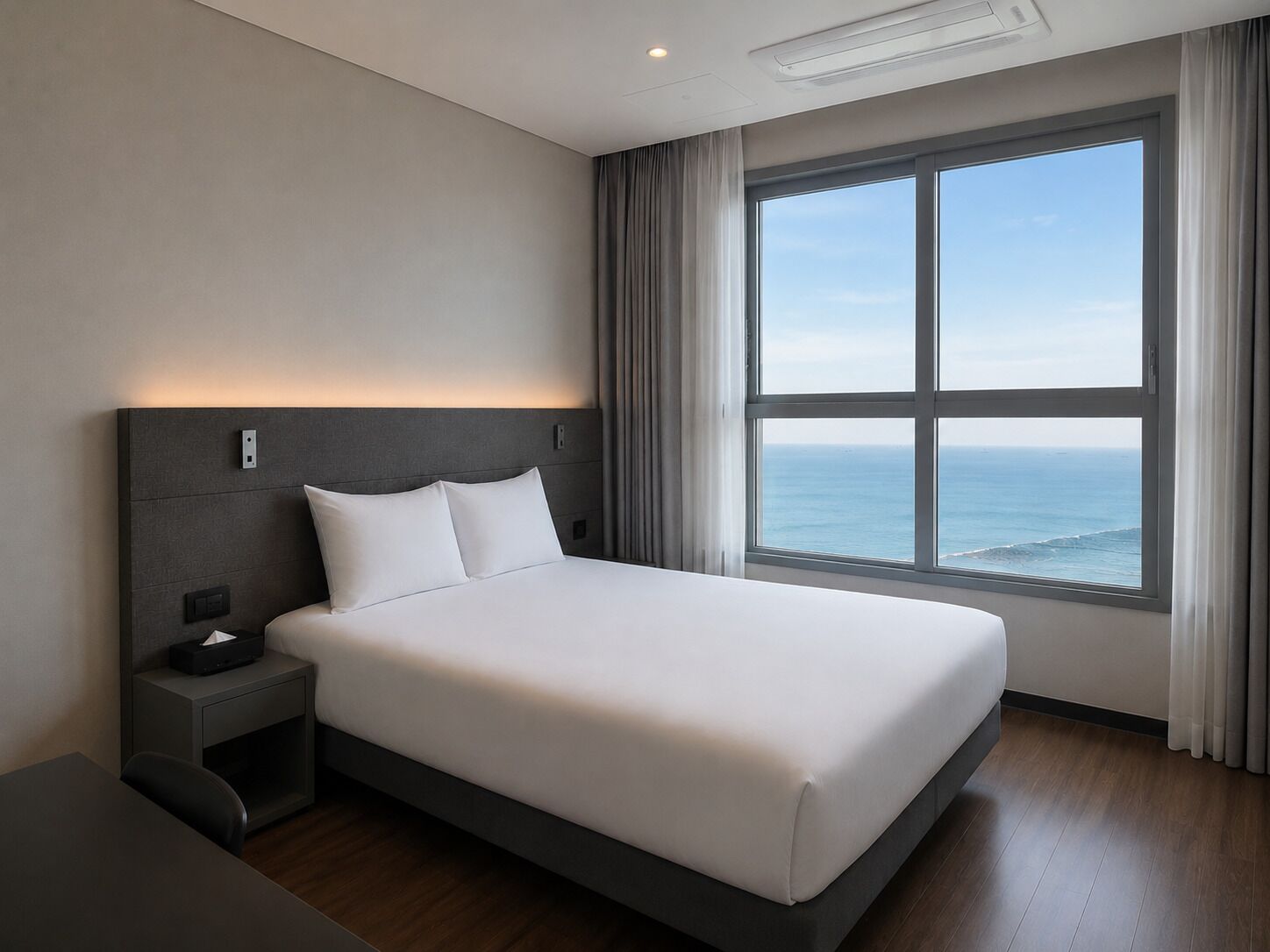 Habitación de hotel moderna con una cama grande, una mesita de noche, un escritorio y vistas al océano.