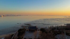 Een uitzicht op de kust met een traditioneel paviljoen, kalm water en een verre stadshemel.